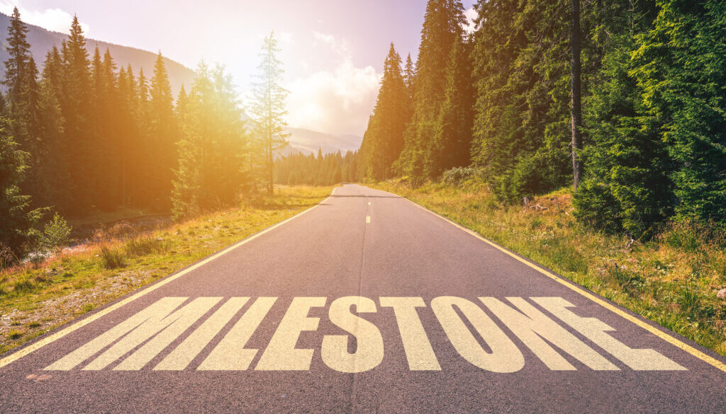 Asphalt road with arrow guideline and Milestone letters painted on the surface. An image of a road milestones are representative of success in the future goal. Road to success with light of the sun